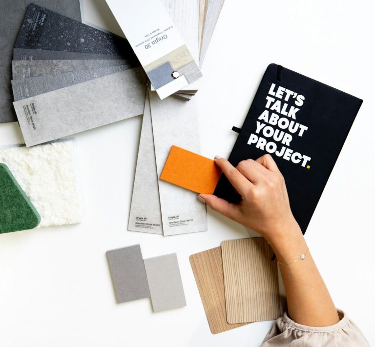 A hand selecting a colour swatch from various material samples and a project notebook.